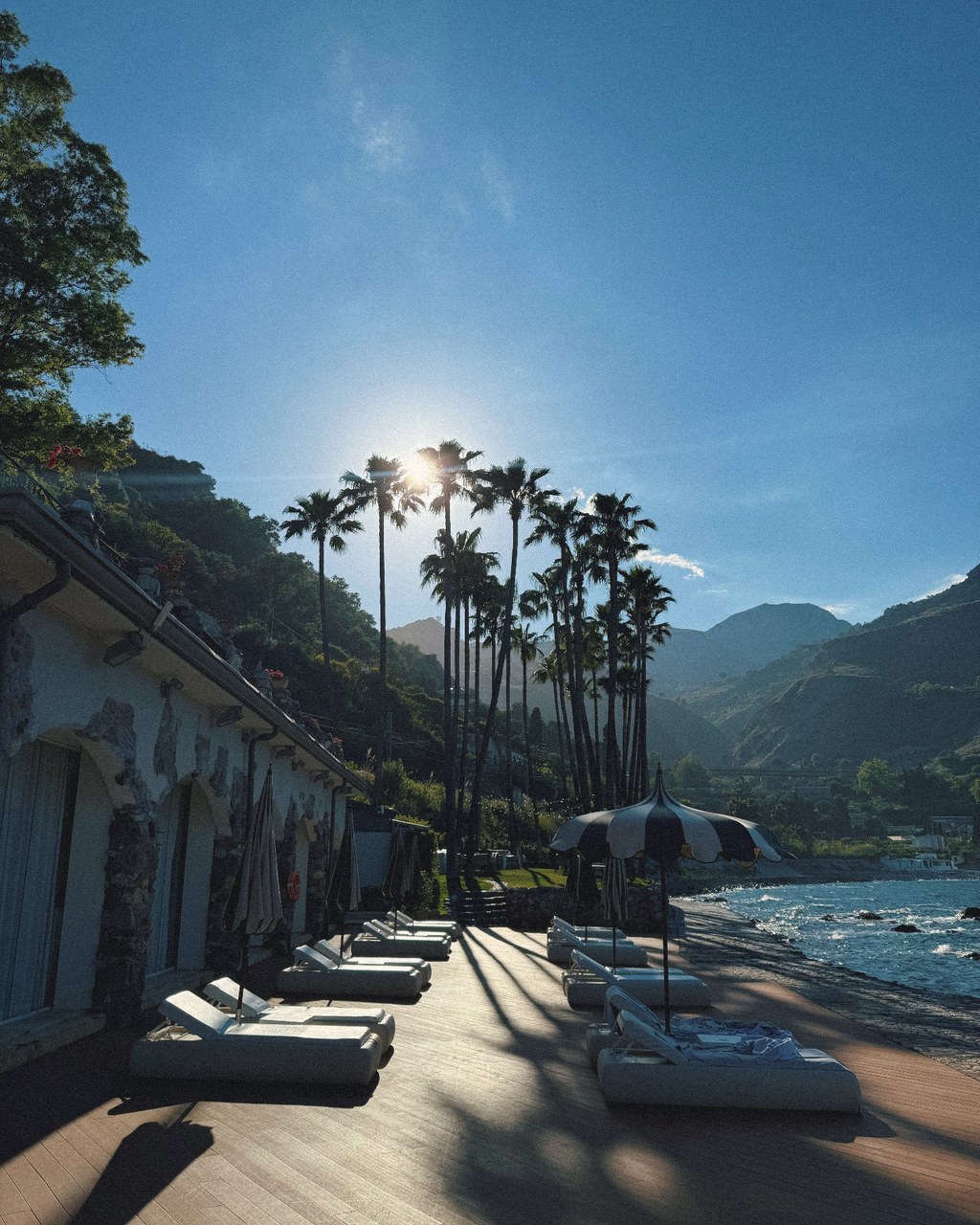 Sun setting behind tall palms over the loungers of a tucked-away beach club