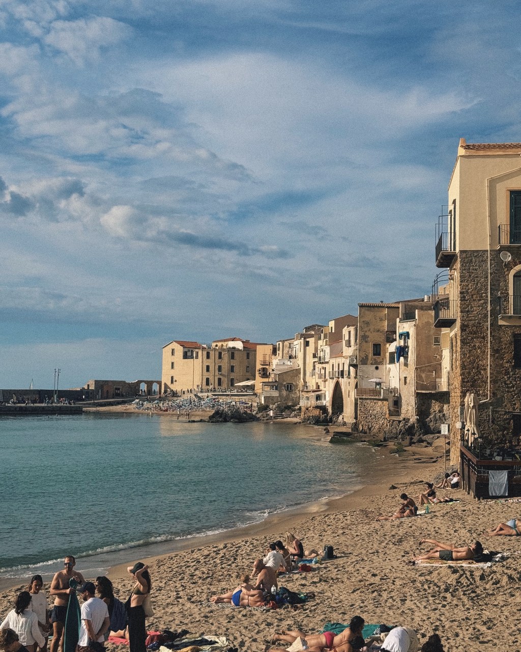 Golden-hour light on an old Sicilian seaside town above a quiet beach