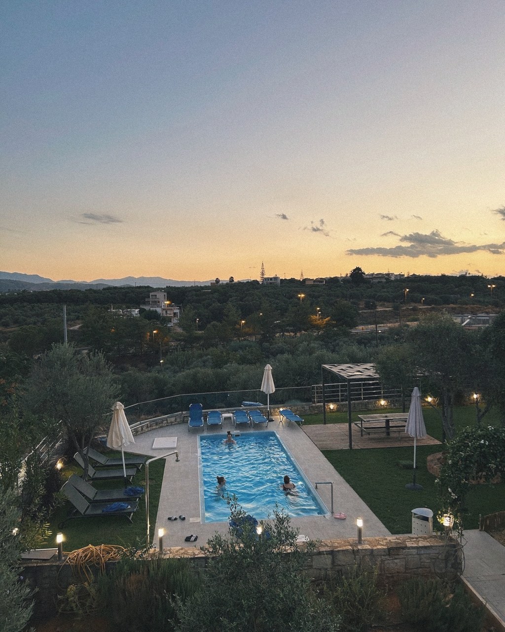 A villa pool glowing at dusk as the sun sets over the Cretan hills